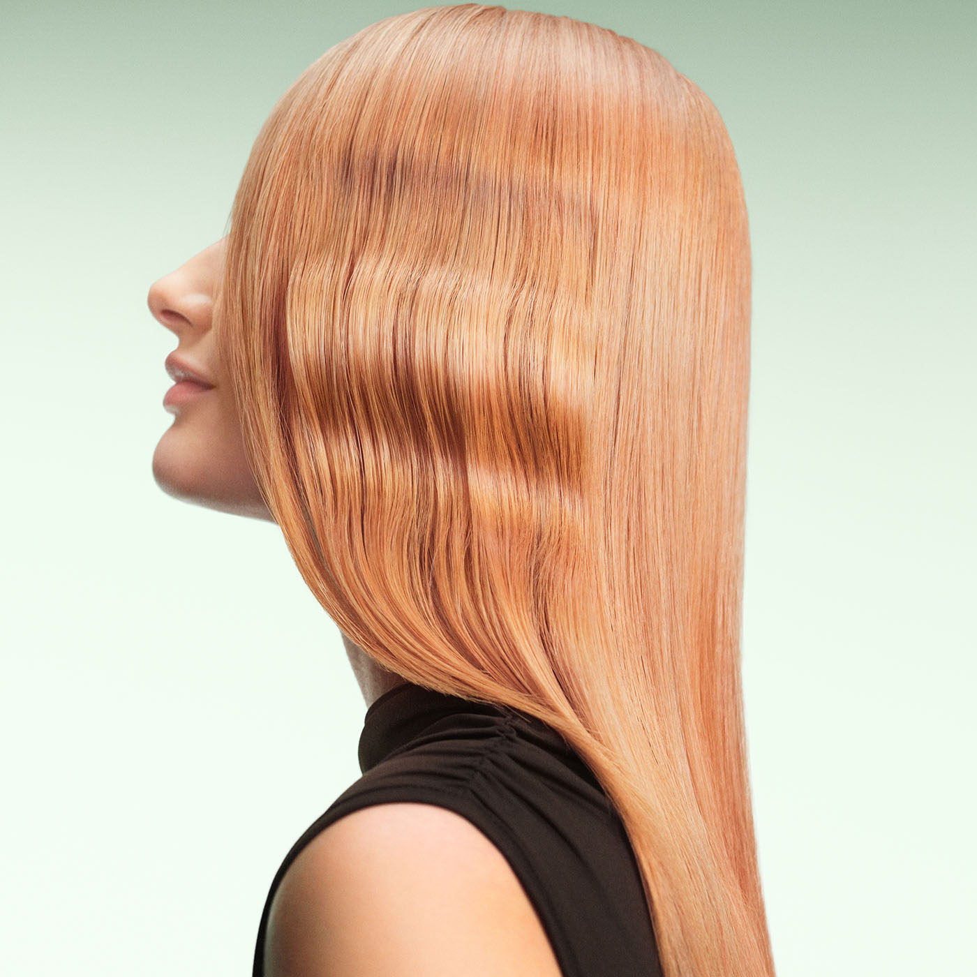 Model with long, wavy, strawberry blonde glossy hair on green background.