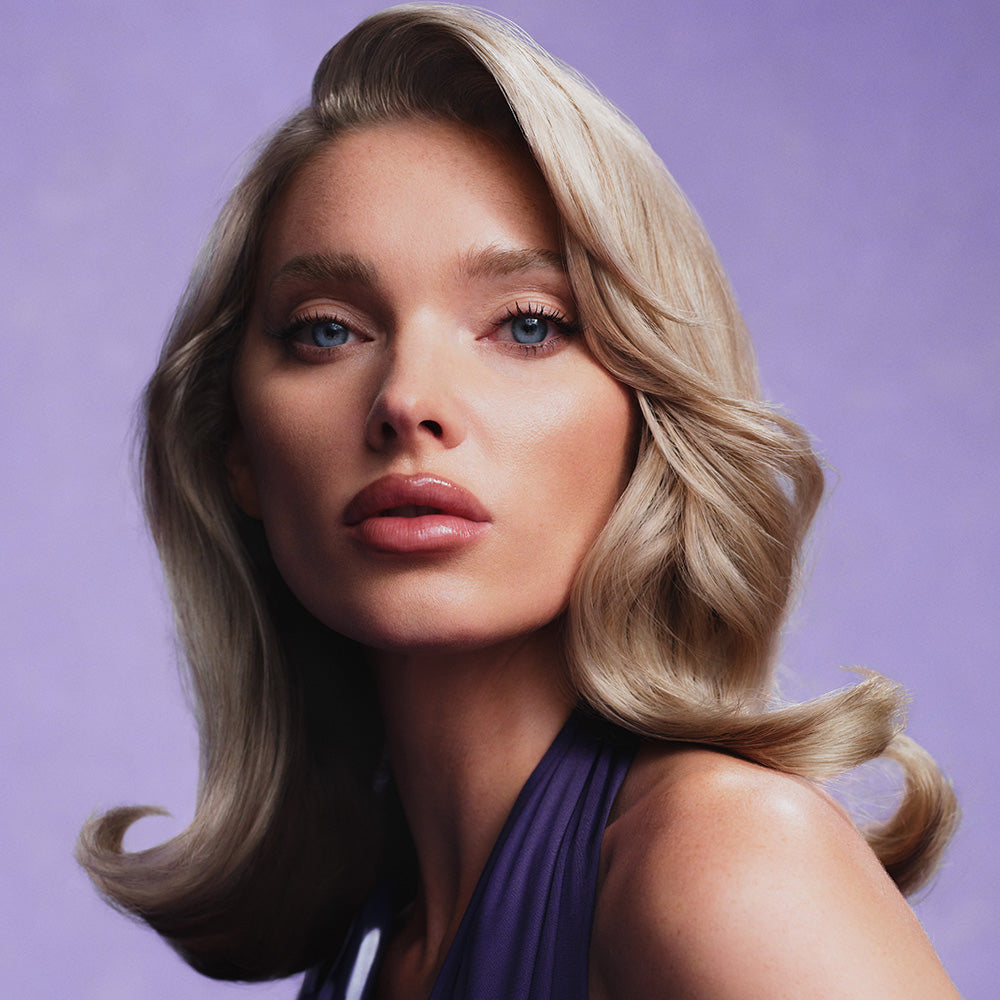 Elsa Hosk with short blonde hair dressed in a purple dress against a purple background